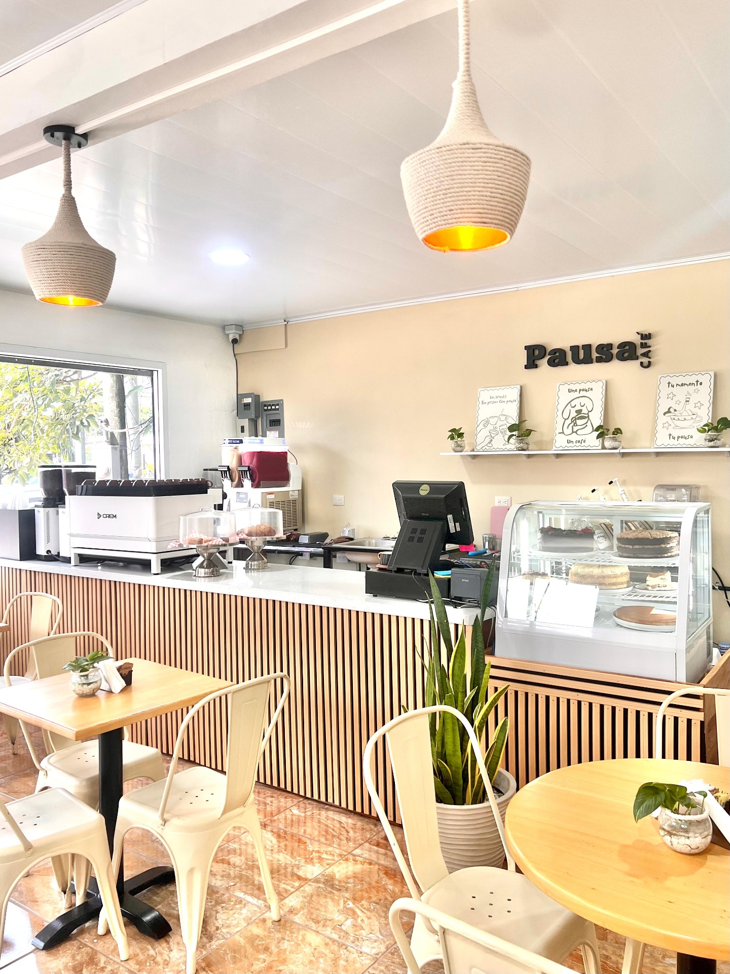 Interior de Pausa Café: mostrador, vitrina de postres, mesas y sillas con iluminación cálida y ambiente acogedor